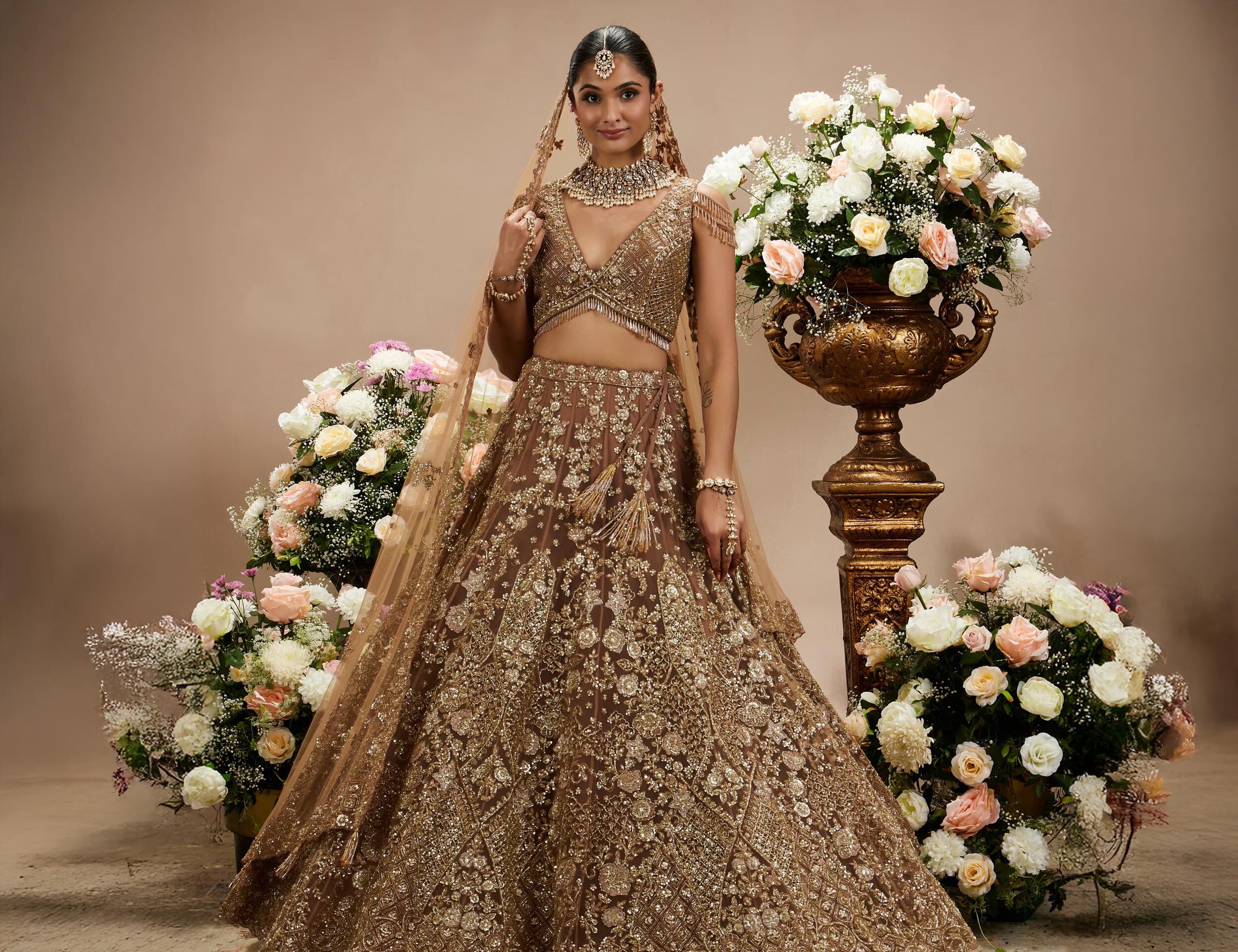 Woman modeling an elaborate gold and brown bridal lehenga with heavy threadwork, showcasing a stunning wedding style.